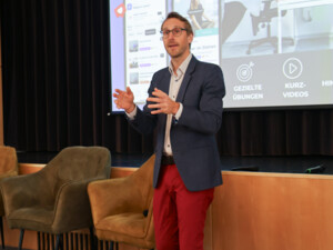 Ein Vortragender steht vor einer großen Präsentationsfolie und erklärt Inhalte zu digitalen Anwendungen für Gesundheit und Bewegung.