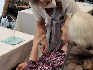 Pflegemitarbeiterin beugt sich nach vorne, um mit einer im Rohlstuhl sitzenden Bewohnerin zu reden.