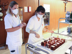 Zwei Pflegerinen bringen gerade den Kuchen auf einem Rollwagen in den Generationensaal. Eine Pflegerin zündet die Geburtstagskerzen an.