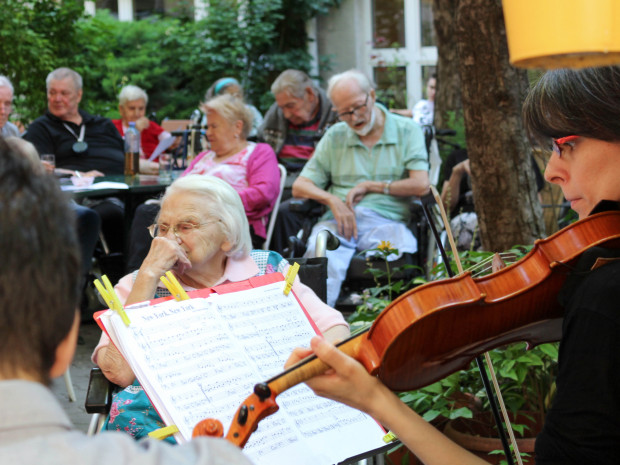 BewohnerInnen sitzend vor MusikerInnen im Garten des Hauses.