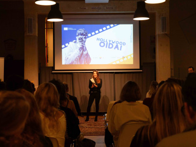 Julia Rusin, die Projektmanagerin des DBY-Projekts in ÖJAB, stehend vor Publikum und das Projekt und die Kurzfilme präsentierend.