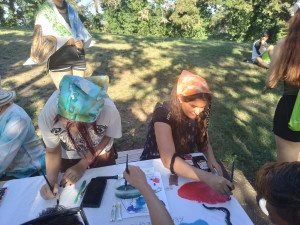 Two young girls are painting pictures outdoors with watercolors.