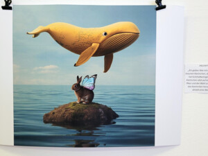 Ein surreal wirkendes digitales Bild zeigt ein Kaninchen mit bunten Schmetterlingsflügeln auf einem kleinen Felsen im Meer. Über ihm schwebt ein gelber Wal, der in Form und Farbe an eine Banane erinnert. Die Szene wurde mithilfe eines Prompts von Jugendlichen mit KI gestaltet.