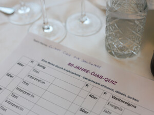 Ein Quizblatt mit dem Titel "80 Jahre ÖJAB" liegt auf einem Tisch neben Gläsern und Getränken.