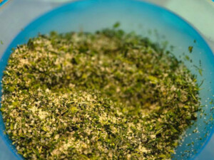 Blaue Schüssel mit grobem Salz und fein gehackten grünen Kräutern; Mischung für hausgemachtes Kräutersalz.