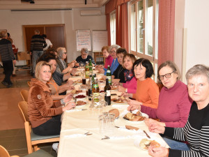 Eine große Gruppe von ehrenamtlichen Mitarbeitenden sitzt an einer langen, festlich gedeckten Tafel, genießt das Essen und blickt lächelnd in die Kamera.