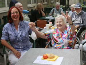 Pflegemitarbeiterin mit Bewohnerin handhaltend und sitzend im Garten.