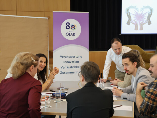 Mehrere Teilnehmende sitzen an einem Tisch, diskutieren miteinander und arbeiten gemeinsam an Themen rund um gesunde Führung; im Hintergrund ist ein ÖJAB-Rollup sichtbar.