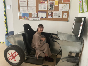 Japanische Ausstauschstudentin sitzend in einem Modellauto aus Blech, ausgestellt am BPI der ÖJAB - Ausbildungszentrum Wien. Foto: Chinami Okuyama.