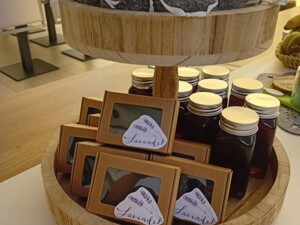 Zweistöckige Holz-Etagere mit handgemachten Lavendelsäckchen, dekorativen Seifen in Kartonschachteln mit Sichtfenster und Flaschen mit Lavendelsirup. Die Produkte stehen auf einem Tisch zur freien Spende bereit.