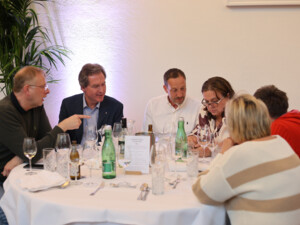 Eine Gruppe von Teilnehmenden sitzt an einem Tisch, spricht miteinander und blickt auf Unterlagen.