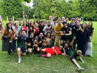 Eine große Gruppe jubelnder Personen, darunter Fußballspieler:innen in schwarzen Trikots mit grünem Muster, feiert die Verleihung des Fairplay-Preises. Einige halten Dosen, andere machen Selfies.