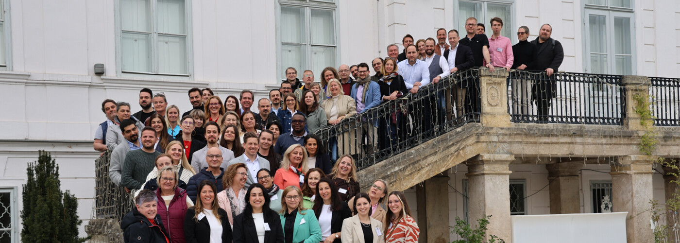 Große Gruppe von Teilnehmenden steht auf einer Treppe vor einem Gebäude und blickt in die Kamera für ein Erinnerungsfoto.