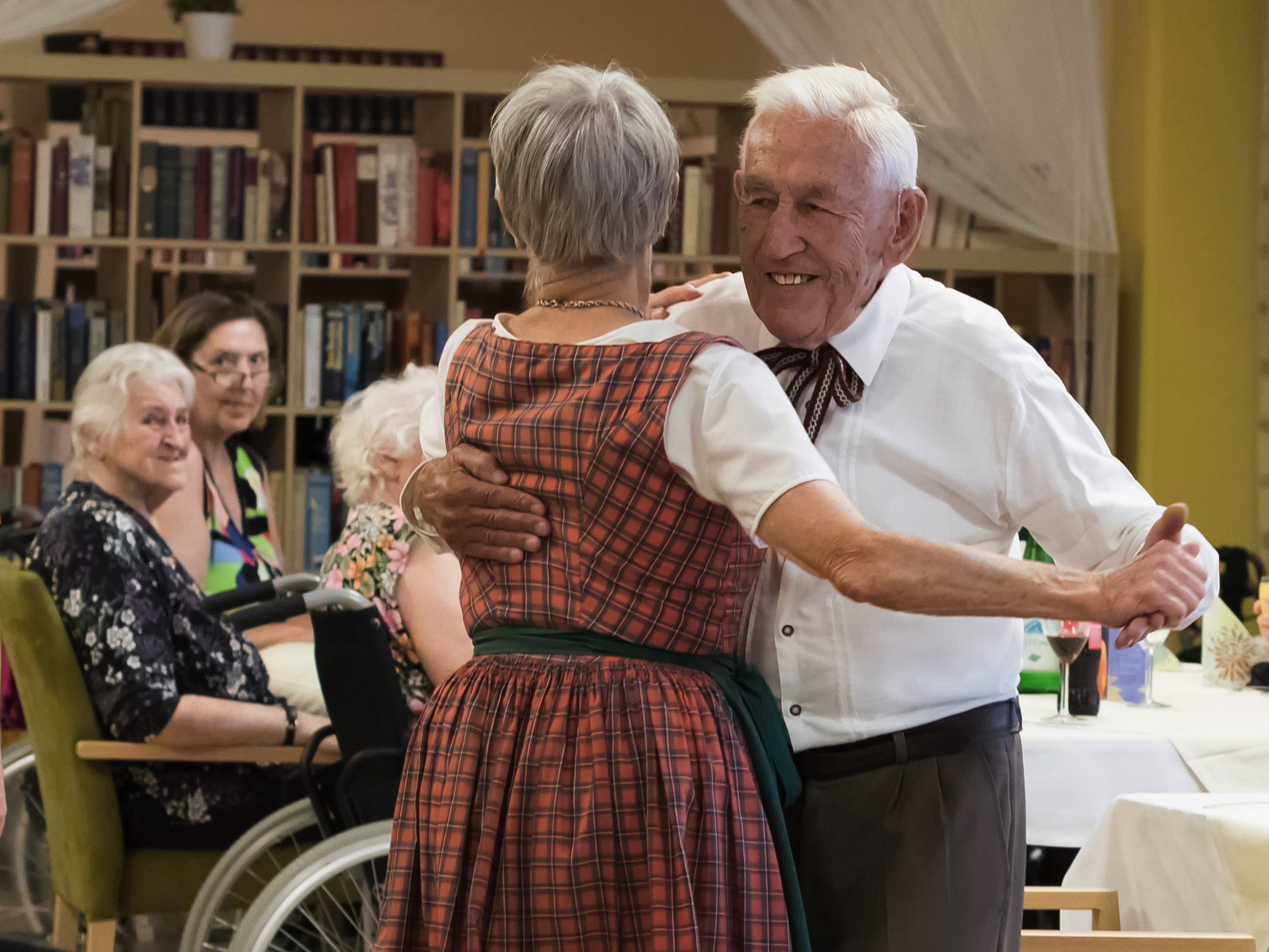 Symbolbild SeniorInnen im Vordergrund tanzend und sitzend im Hintergrund.