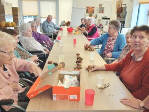 Eine große Gruppe Senior:innen sitzt an einem Tisch, auf dem zahlreiche frische Steinpilze liegen. Eine geöffnete Schuhschachtel dient als Behälter.