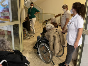 BewohnerInnen im Rohlstuhl sitzend gemeinsam mit PflegemitarbeiterInnen wartend vor dem Lift im alten ÖJAB-Haus Neumargareten.