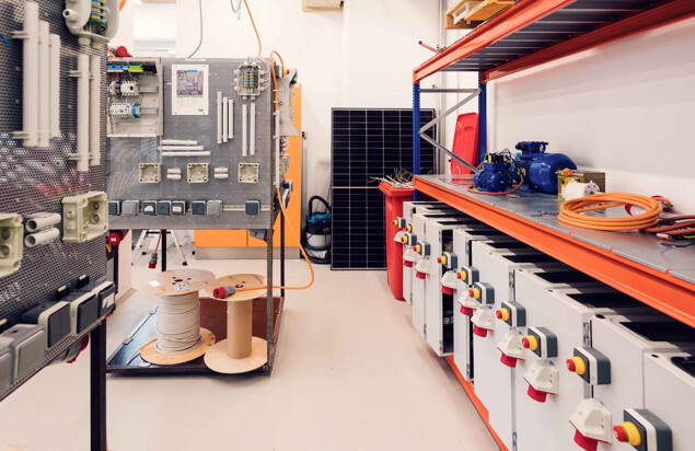 Ein heller Technikraum mit Elektroinstallationswänden, Kabelrollen, Steckdosenmodulen, Solarpanel, Motoren und weiteren Bauteilen für praktische Übungen in technischen Kursen. Foto: www.inframe.at