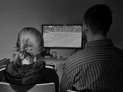 Mann und Frau sitzend vor Fernseher, von hinten aufgenommen.