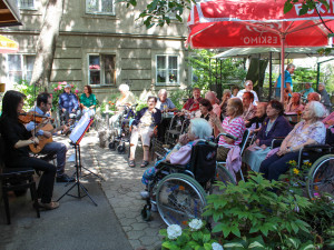 BewohnerInnen und Angehörige sitzend vor zwei MusikerInnen bei einem Gartenkonzert im ÖJAB-Haus Neumargareten.