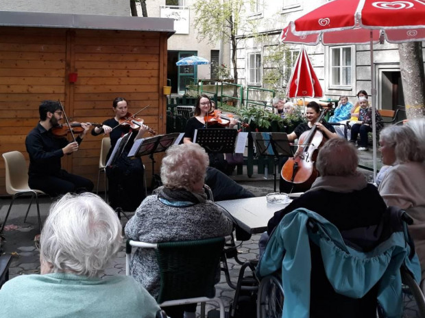 BewohnerInnen sitzend vor MusikerInnen im Garten des Hauses.