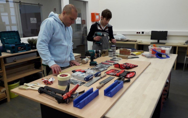 Teacher and apprentice standing in front of a workbench with tools.