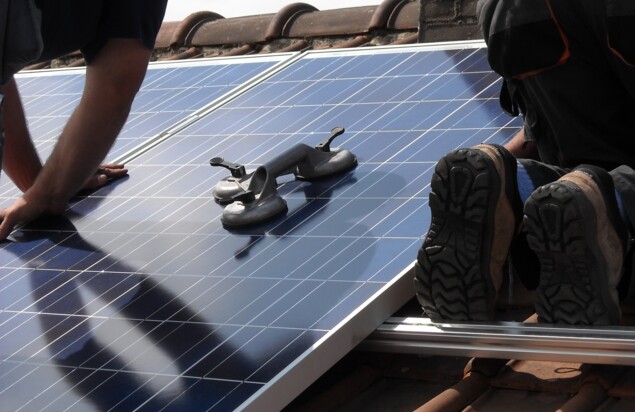 Photovoltaik-Anlage auf einem Dach und darauf arbeitende Techniker.
