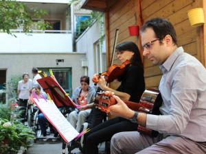 Nahaufnahme der Musikerin Irene Malizia an der Violine und Angelos Tatone an der Gitarre im Garten des Wohn- und Pflegewohnheims.