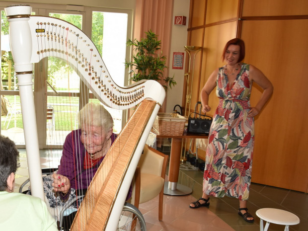 BewohnerInnen des Pflegewohnhauses ÖJAB-Haus St. Franziskus sitzend an der Harfe und Musikerin Sabine James stehend im Hintegrund.