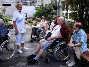 BewohnerInnen und Angehörige sitzend, neben Pflegemitarbeiterin stehend, bei einem Gartenkonzert im ÖJAB-Haus Neumargareten.