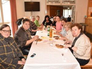 Eine große Gruppe von Personen sitzt gemeinsam an einem langen Tisch, isst und unterhält sich. Die Stimmung wirkt fröhlich und familiär.