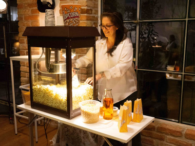 Person stehend vor einer Popcorn-Maschine, Popcornsackerl mit frischem Popcorn befüllend.