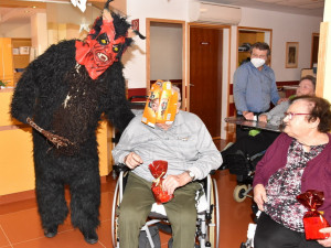 Krampus stehend neben BewohnerInnen sitzend. Im Hintergrund Angehöriger stehend.
