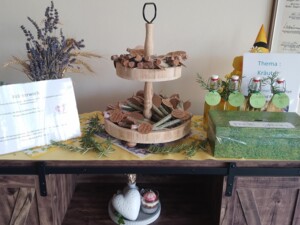 Ausstellung im Haus St. Franziskus: dekorierter Tisch mit Rosmarinzweigen, beschrifteten Fläschchen und Spendenbox "Freie Spende" - Resultat der Kräuterwoche.