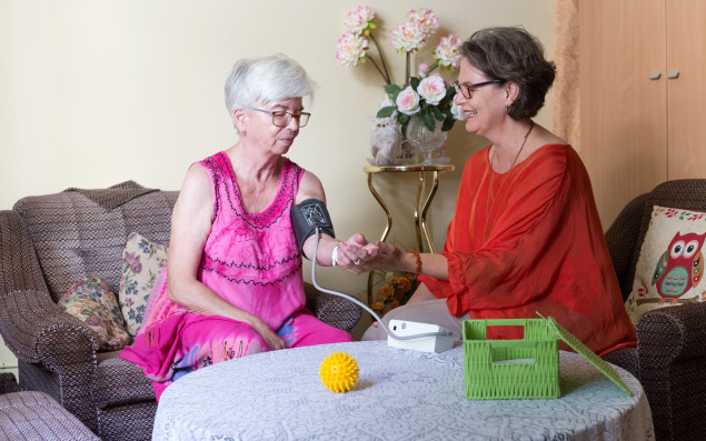 Pflegerin misst den Blutdruck einer Bewohnerin in Heimzimmer.