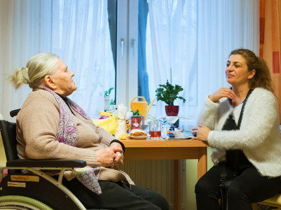 Bewohnerin und Betreuerin sitzend gegenüber an einem Tisch und miteinander redend.