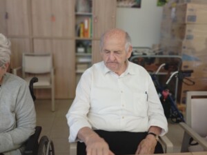 Ein älterer Mann sitzt am Tisch und formt Keksteig mit der Hand. Vor ihm liegen ein Glas, etwas Teig und eine Ausstechform.