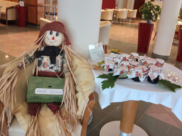 Ein Tisch im Eingangsbereich ist mit Gläsern hausgemachter Marmelade dekoriert. Daneben sitzt eine herbstlich gekleidete Strohpuppe mit einer Spendenbox auf dem Schoß.