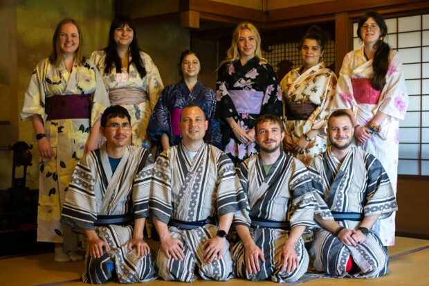 Zehn junge Teilnehmer:innen des Österreichisch-Japanischen Jugendaustauschs tragen Yukatas und posieren gemeinsam in einem traditionell eingerichteten japanischen Raum.