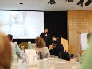 Eine Referentin steht mit Mikrofon vor einer Präsentationsfolie und spricht über Schlaf und Regeneration.