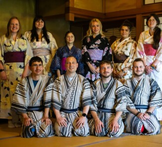 Zehn junge Teilnehmer:innen des Österreichisch-Japanischen Jugendaustauschs tragen Yukatas und posieren gemeinsam in einem traditionell eingerichteten japanischen Raum.