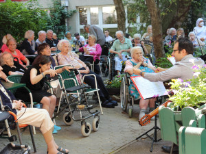 BewohnerInnen und Angehörige sitzend vor zwei MusikerInnen bei einem Gartenkonzert im ÖJAB-Haus Neumargareten.
