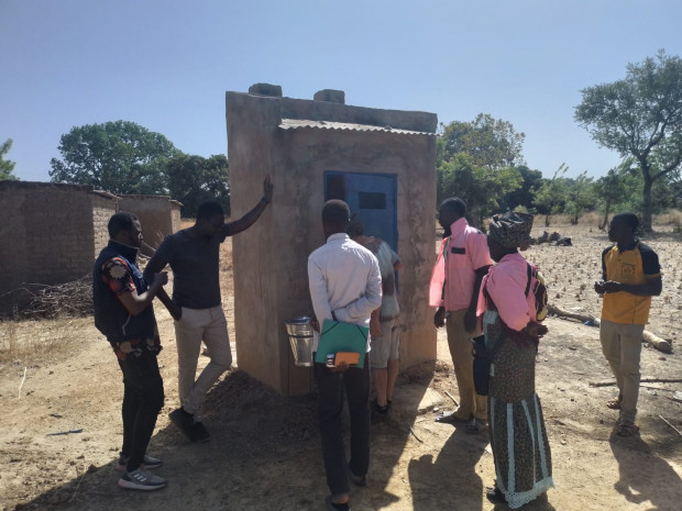 Bewohner:innen der Gemeinde Samba und NGO-Mitarbeiter:innen stehen rund um eine Kompostlatrine und Handwaschanlage in der Geminde von Samba.