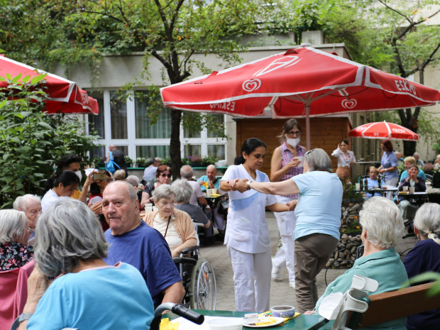BewohnerInnen sitzend im Vordergrund und tanzend mit Mitarbeiterin im Hintergrund beim Grillheurigen im Garten des Hauses.