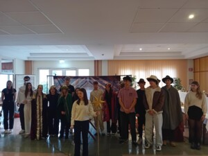 Eine Gruppe von etwa 18 Jugendlichen steht gemeinsam vor der Kulisse des Krippenspiels. Einige tragen Kostüme als Könige, Hirten, Engel oder andere Rollen, andere sind in Alltagskleidung. Eine Person hält einen goldenen Sternstab.