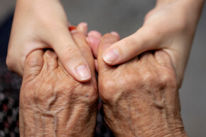 Nahaufnahme von zwei jungen Händen, die sanft die beiden Hände einer älteren Person umschließen. Die Szene vermittelt Fürsorge, Vertrauen und generationenübergreifende Unterstützung.