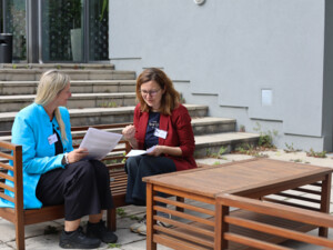 Zwei Teilnehmende sitzen auf einer Bank im Außenbereich und diskutieren anhand von Unterlagen.
