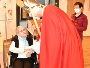 Bewohnerin sitzend mit Nikolo und Zivildiener stehend. Im Hintergrund eine Pflegemitarbeiterin des Hauses.
