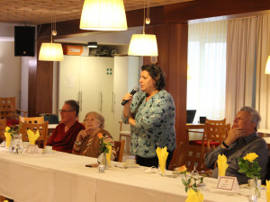 Leiterin Monika Antl-Bartl, sehtend in der Mitte vor einem Tisch,  sprach ein paar Worte zur Begrüßung an die anwesenden Gäste.