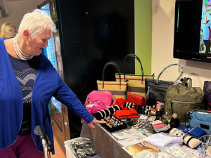Bewohnerin stehend links zeigt auf Präsentiertisch mit Accessoires rechts.