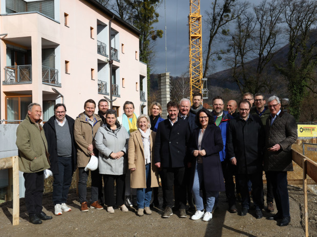 Gruppenbild aller Beteiligten bei der Baustelleneröffnung für das ÖJAB-Pflegewohnhaus Salzburg, im Hintergrund die derzeitige ÖJAB-Senior:innenwohnanlage Aigen. 